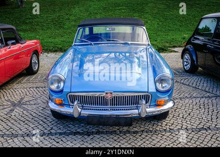 Lissabon, Portugal - 20. Januar 2024: Ein klassischer, himmelblauer MGC Roadster mit Chromdetails, der auf einem Kopfsteinpflasterweg in der Nähe eines grünen Parks parkt. Stockfoto