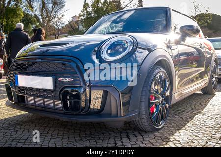 Lissabon, Portugal - 20. Januar 2024: Elegante, komplett schwarze Mini John Cooper Works parkt an sonnigen Tagen auf einem Kopfsteinpflasterweg in der Nähe des grünen Parks. Stockfoto