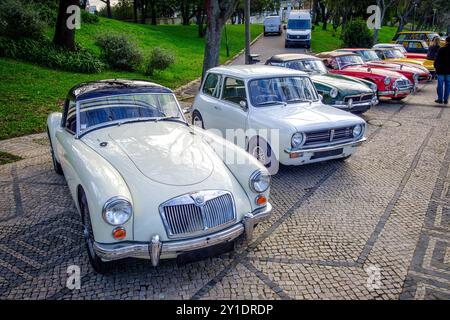 Lissabon, Portugal - 20. Januar 2024: Eine Reihe von Oldtimern der Marken MG und Mini Cooper und andere parkten auf einer kopfsteingepflasterten Auffahrt in der Nähe des grünen Parks. MGA, 1973 Morris Mini Clubman, MGC Roadster, MGA TWIN CAM und andere. Stockfoto