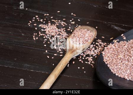 Reiskörner auf einem Tisch verstreut mit Körnern in einem Holzlöffel und einem weiteren Teil in einem schwarzen Teller. Stockfoto