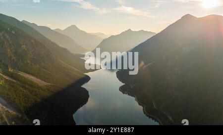 Wenn die Sonne über Plansee untergeht, erleuchtet goldenes Licht das ruhige Wasser, umgeben von majestätischen Bergen. Die ruhige Landschaft lädt zum friedlichen Beisammensein ein Stockfoto