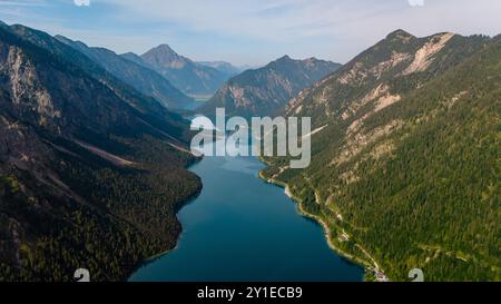 Über dem atemberaubenden türkisfarbenen Wasser des Plansees erheben sich majestätische Berge steil, umgeben von üppigem Grün. Der ruhige See reflektiert den Himmel und schafft eine ruhige Landschaft, die perfekt für Naturliebhaber ist. Stockfoto