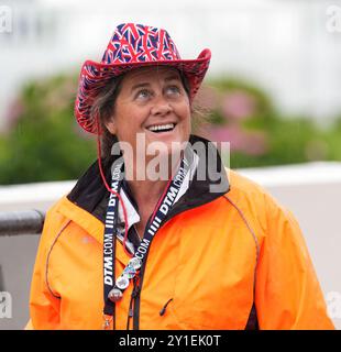 Ein lächelnder Rennmarschall bei Goodwood Revival, einem fesselnden Motorsport-Event im Vintage-Stil. Mit orangefarbener wasserdichter Jacke und union Flag (Jack) Cowboyhut. Stockfoto