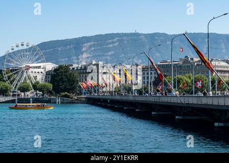 Genf, Schweiz - 28. Juli 2024: Mont-Blanc-Brücke und Schweizer Fahnen über dem Genfer See. Autos und Leute auf der Brücke Stockfoto