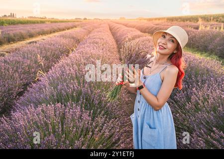 Ein Porträt einer jungen Frau, die Lavendelblumen sammelt und einen Blumenstrauß auf einer lila Sommerwiese kreiert. Stockfoto