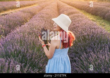 Ein Porträt einer jungen Frau, die Lavendelblumen sammelt und einen Blumenstrauß auf einer lila Sommerwiese kreiert. Stockfoto