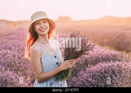 Ein Porträt einer jungen Frau, die Lavendelblumen sammelt und einen Blumenstrauß auf einer lila Sommerwiese kreiert. Stockfoto