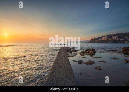 Castiglioncello Reiseziel, Betonpier in der Bucht, Felsen und Meer bei Sonnenuntergang. Lage in Baia del Quercetano. Provinz Livorno, Toskana regi Stockfoto