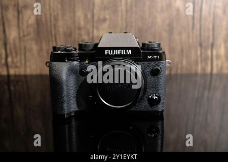 Newcastle UK: 19. Juni 2024: Kamera Fujifilm X-T1 mit einem schwarzen Körper auf einer reflektierenden Oberfläche vor einem hölzernen Hintergrund in einem gut beleuchteten Studio-Set Stockfoto