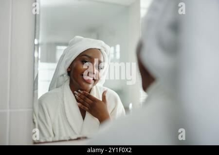 Lächelnde Frau in Bathrobe, die Spiegel ansieht Stockfoto
