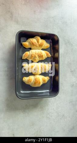Frisch gebackene goldene Croissants auf einem schwarzen Tablett auf hellgrauer Oberfläche Stockfoto