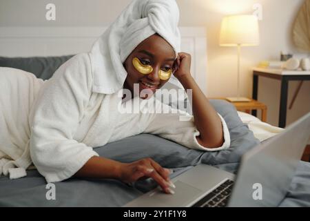 Im Bademantel ruhen, mit Augenflecken, die auf das Notebook schauen Stockfoto