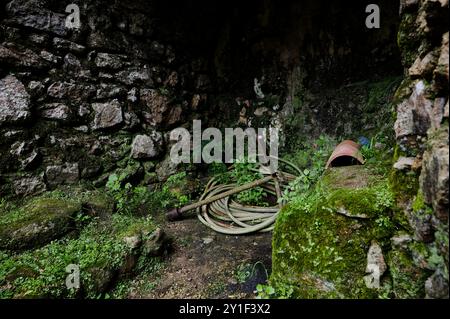 Eine versteckte Ecke in der Nähe der alten Steinmauern in Quinta da Regaleira, wo ein alter Gartenschlauch und Terrakotta-Topf ruhen. Stockfoto