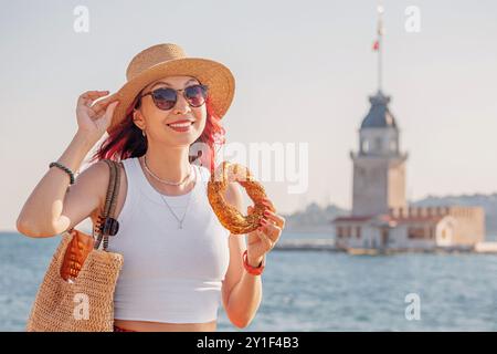 Ein Mädchen genießt einen frischen Simit Bagel aus einem Café in Istanbul, mit dem berühmten Maiden's Tower und dem Bosporus im Hintergrund. Stockfoto