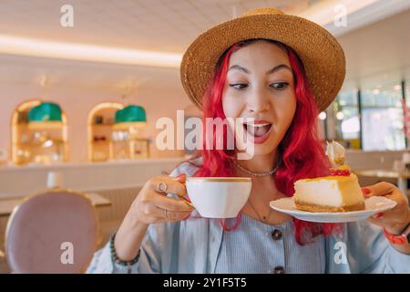 Eine junge Frau genießt gerne ein Stück Kuchen in einem Café, lächelt, während sie ihren Kaffee schlürft und positive Energie ausstrahlt Stockfoto