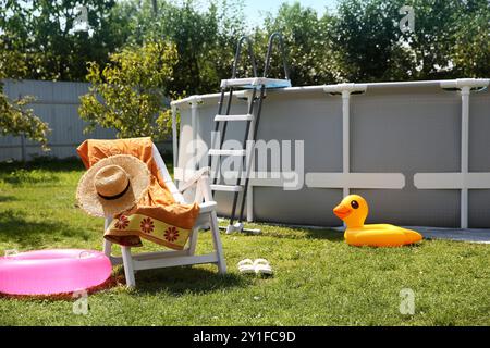 Oberirdischer Swimmingpool, Klappstuhl, Handtuch, aufblasbare Ringe und Hut im Hinterhof Stockfoto