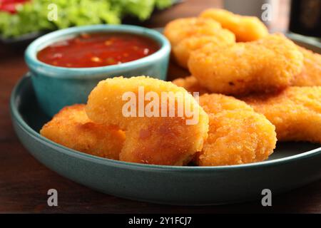 Teller mit heißer Chili-Sauce und Nuggets auf Holztisch, Nahaufnahme Stockfoto