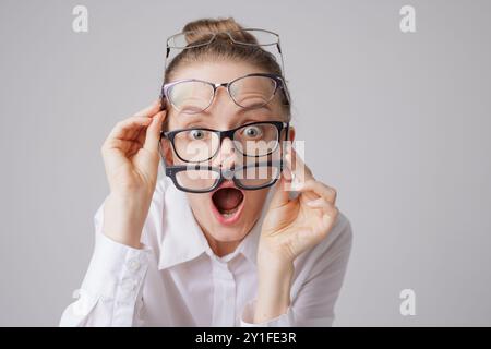 Überraschte Frau in mehreren Brillenpaaren mit schockiertem Ausdruck auf weißem Hintergrund, Astigmatismus-Konzept Stockfoto