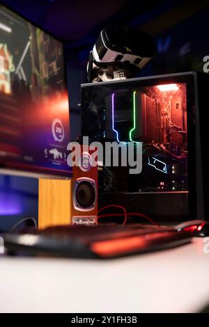 RGB-beleuchtete Teile am geöffneten Gaming-PC-Tower neben Tastatur, Stereo-Lautsprechern, Display und High-Tech-VR-Headset in leerem Apartment. Computer mit moderner Hardware, Monitor und Virtual-Reality-Brille Stockfoto