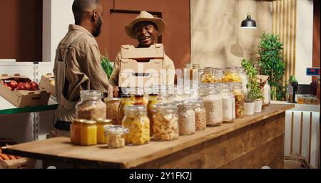 afroamerikanischer Lieferant, der dem Händler frische Produkte in Kisten gibt und an der Wiederauffüllung von Waren mit frisch geernteten Waren arbeitet. Landwirt und Lieferant arbeiten bei der Lieferung von Ladengeschäften zusammen. Kamera 2. Stockfoto