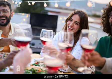 Treffen von fröhlichen jungen Freunden, die mit Rotweinglas getostet werden, um die Sommerparty auf dem Dach zu feiern. Stockfoto