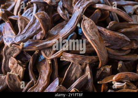 Getrocknete Johannisbrotschoten. Haufen Johannisbrotfrucht-Schoten am Marktstand. Draufsicht, Nahaufnahme Stockfoto