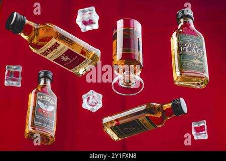 Vier Whiskyflaschen und ein Glas Whisky zwischen Eiswürfeln vor rotem Hintergrund Stockfoto