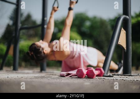 Frau, die im Freien mit Fitnessgeräten mit rosafarbenen Kurzhanteln und Widerstandsbändern trainiert Stockfoto