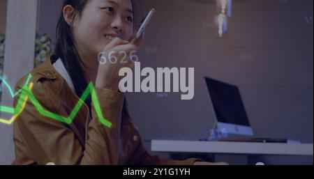 Abbildung von Diagrammen und Datenverarbeitung über asiatische Geschäftsfrau, die auf dem Smartphone spricht Stockfoto