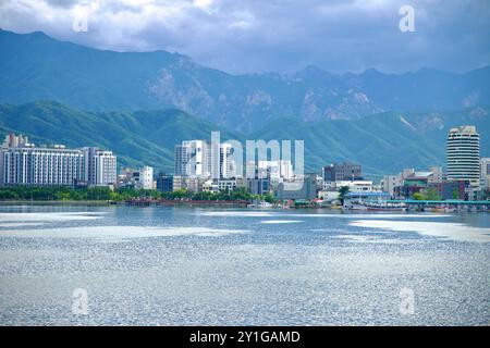 Sokcho, Südkorea - 28. Juli 2024: Ein breiter Blick auf die Skyline von Sokcho vor den zerklüfteten Taebaek Mountains mit dem ruhigen Wasser von Cheong Stockfoto