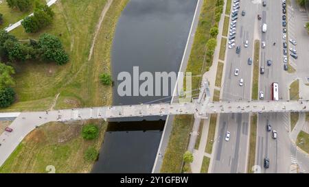 Aus der Vogelperspektive auf eine Fußgängerbrücke über den Fluss und die Menschen, die während des sonnigen Sommertages auf dem Fluss spazieren gehen Stockfoto