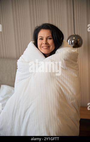 Glückliche Frau hüllt sich in eine flauschige Decke Stockfoto