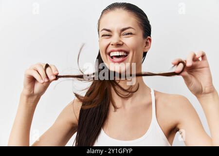 Glückliche Frau, die mit ihren Haaren spielt, fröhlich lächelt, eine sorglose Haltung vor einem sauberen weißen Hintergrund zeigt, von dem das Bild Gefühle vermittelt Stockfoto