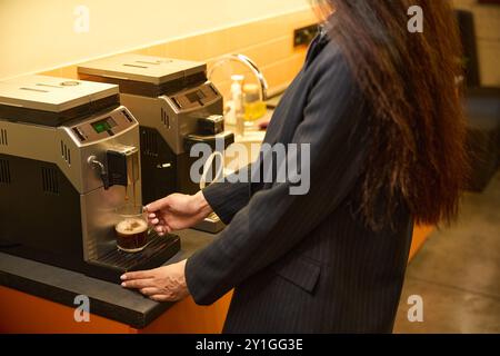 Frau mit langen Haaren macht sich Kaffee in einer kühlen Kaffeemaschine Stockfoto