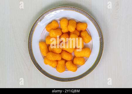 Knusprige Snacks mit Käsegeschmack Cracker Chips auf einem weißen Teller auf einer hellen Holzoberfläche. Draufsicht. Stockfoto