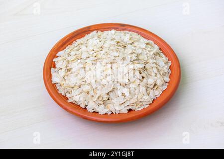 Roher, flacher Reis oder Chira auf einer Tonplatte auf einer hellen Holzoberfläche. Es ist auch bekannt als poha, pohe, aval, Pauwa, sira, Chivda oder Avalakki. Stockfoto