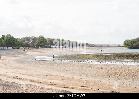 Ein malerischer Blick auf einen felsigen Strand bei Ebbe, mit dem Meer im Hintergrund. Sanfte Wellen am Ufer, und ein paar Leute können beim Erkunden beobachtet werden Stockfoto