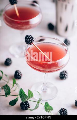 Brombeer-Gin-Cocktail in Martini-Glas mit Obst auf luxuriösem Marmortisch. Getränk für eine elegante Dinnerparty. Stockfoto