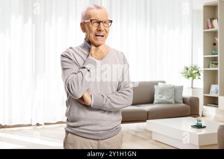 Älterer Mann mit Halsschmerzen, der zu Hause in einem Wohnzimmer steht Stockfoto