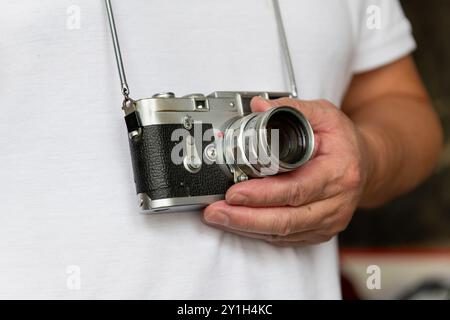 Eine Person, die eine klassische Fotokamera im Vintage-Stil trägt und hält. Stockfoto