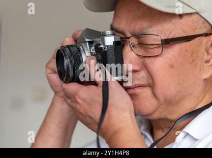 Ein älterer Mann, der eine klassische Spiegelreflexkamera benutzt, um Fotos zu machen. Stockfoto