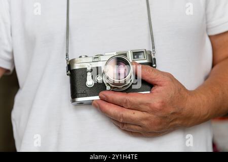 Eine Person, die eine klassische Fotokamera im Vintage-Stil trägt und hält. Stockfoto