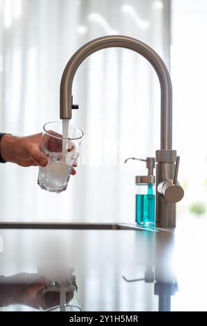 Person, die ein Glas Wasser füllt. Selektiver Fokus auf Glas, vertikale Aufnahme. Stockfoto