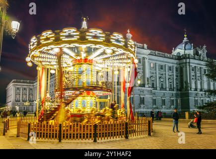 Ein hell beleuchtetes Karussell dreht sich vor dem Königspalast in Madrid, Spanien. Stockfoto