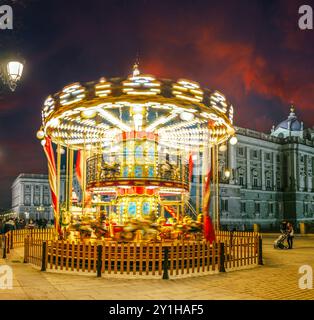 Ein hell beleuchtetes Karussell dreht sich vor dem Königspalast in Madrid, Spanien. Stockfoto