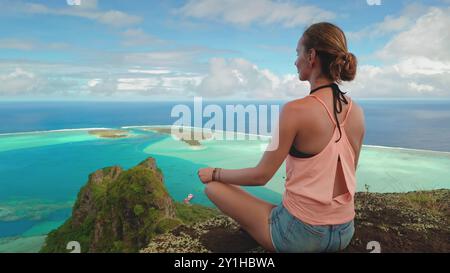 Die junge Frau genießt einen Moment der Ruhe und Ruhe, während sie Yoga auf einer Klippe mit Blick auf ein atemberaubendes tropisches Inselparadies übt Stockfoto