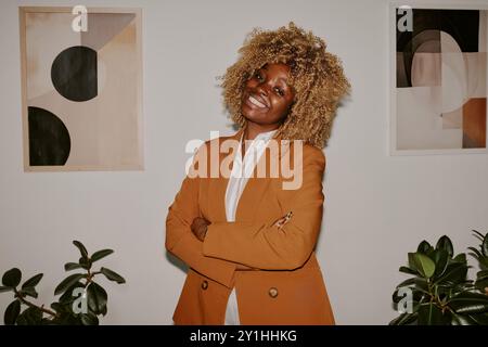 Porträt einer Frau mit lockigem Haar, die breit lächelt und direkt in die Kamera blickt, während sie im Büro posiert Stockfoto