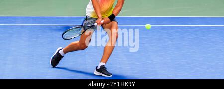Seitenansicht eines männlichen Tennisspielers, der während eines Spiels aggressiv mit zwei Händen auf den Ball schwingt. Stockfoto