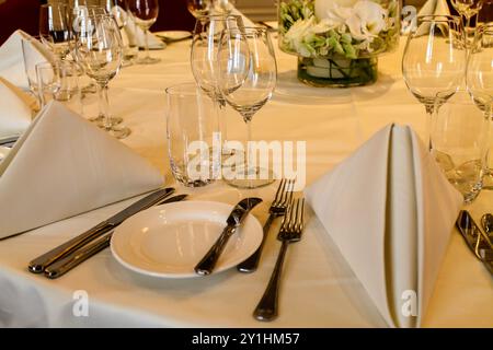 Ein wunderschön gedeckter Esstisch mit eleganten weißen Servietten, Gläsern und Besteck, ordentlich angeordnet. Das Herzstück ist mit frischen Blumen versehen, die einen Stockfoto