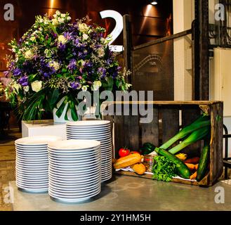 Eine wunderschön angeordnete Ausstellung mit einem großen Blumenarrangement in Violett- und Grüntönen sowie weißen Tellern mit blauen Rändern. A Stockfoto